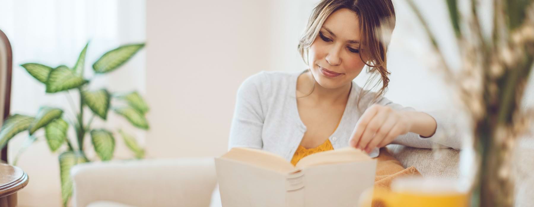 A woman sitting in a well lit living room ready a book
